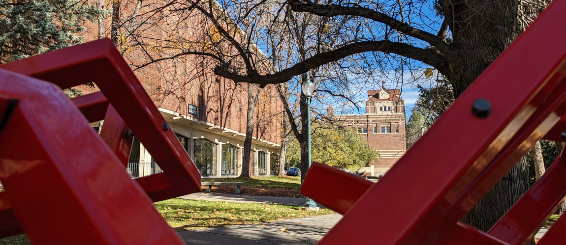 Brick campus buildings framed in the foreground by red metal bars.