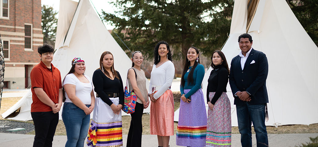 A group of Native American standing in front of teepees. 