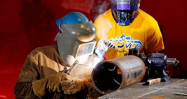 people in full face shield and heavy gloves welding a pipe