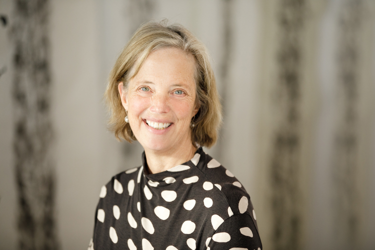 A smiling woman artistically posed, wearing a bold black polka-dot top and with with her head slightly tilted.