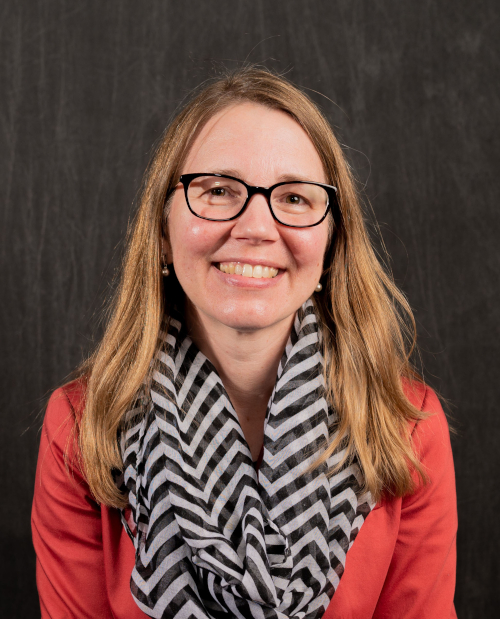 A smiling woman with blonde hair, black glasses, and a striped scarf.