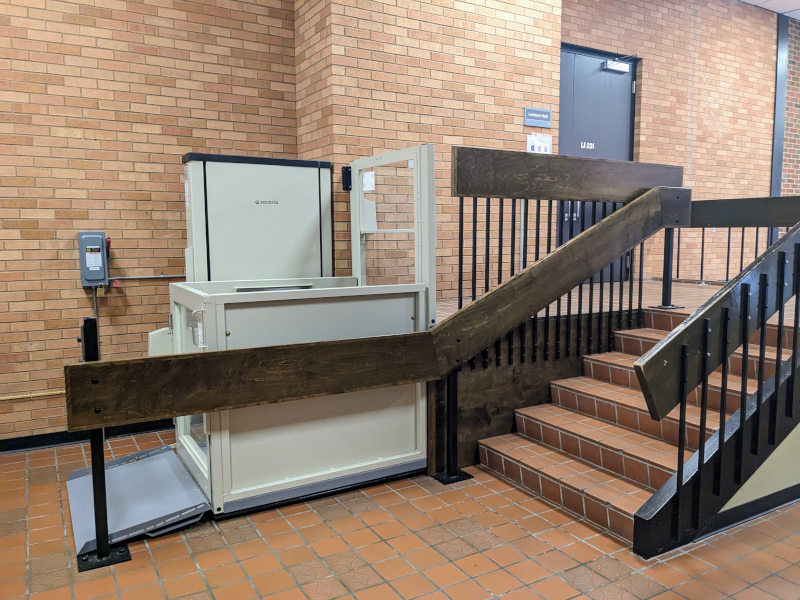 A lift in a lobby, bypassing a half-flight of stairs to get to a door marked "Lecture Hall."