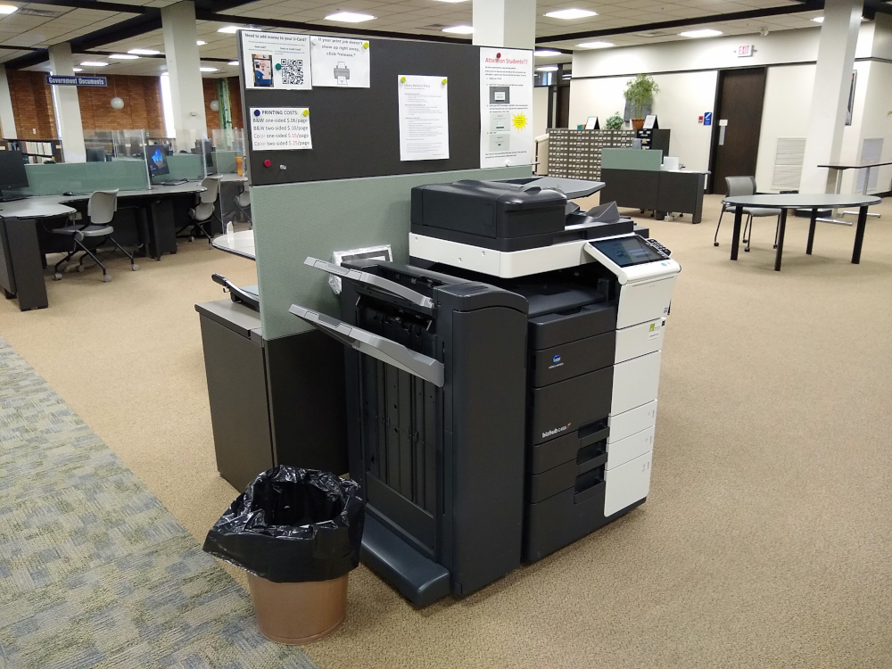 A printer against a green backdrop with an orange brick wall in the distance.