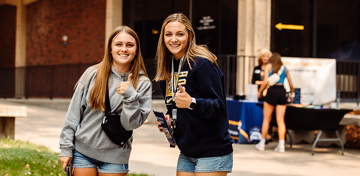 Two students pose with thumbs up.