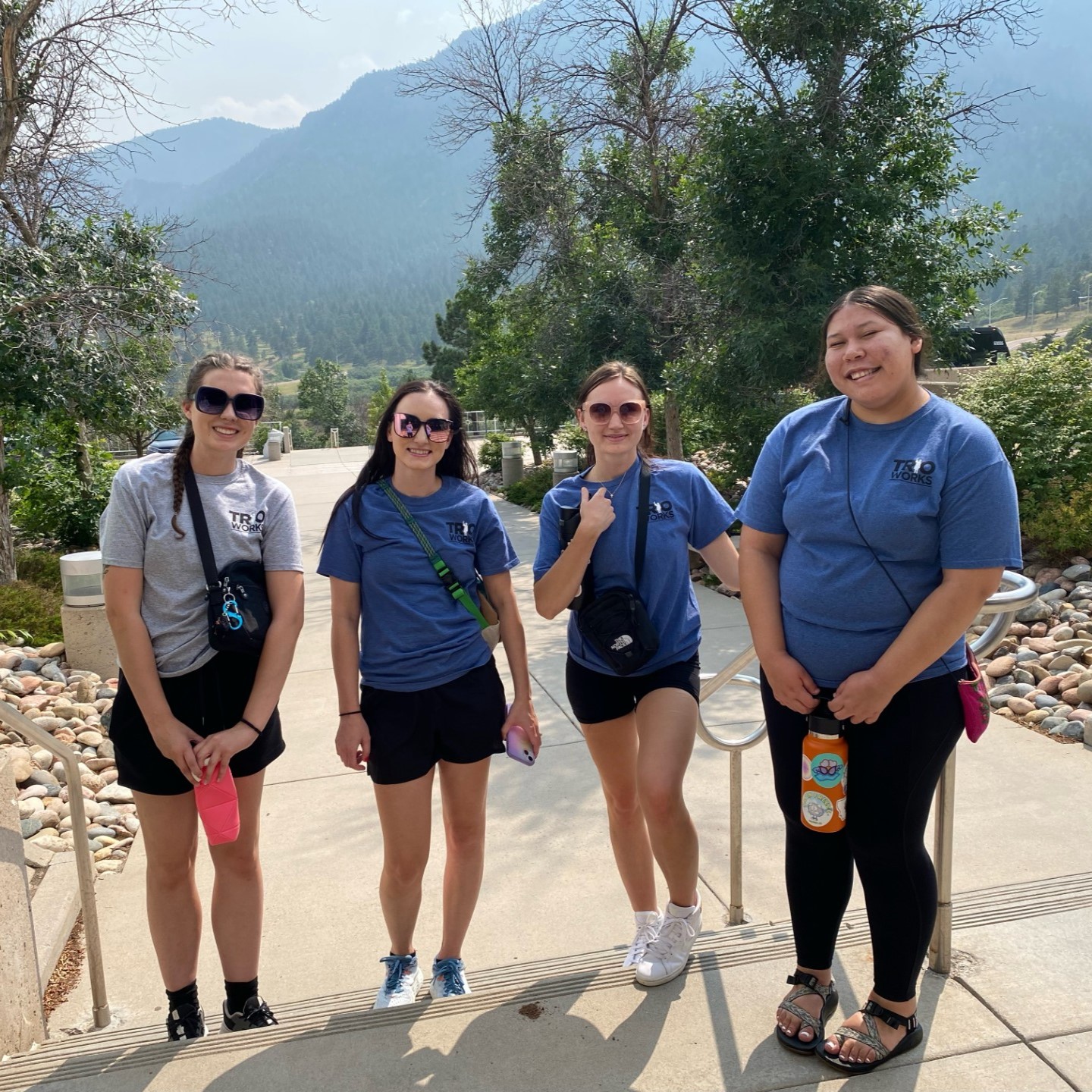 Four students standing at the bottom of stairs wearing "TRIO Works" t-shirts