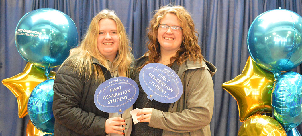 two young women holding "first generation students" signs